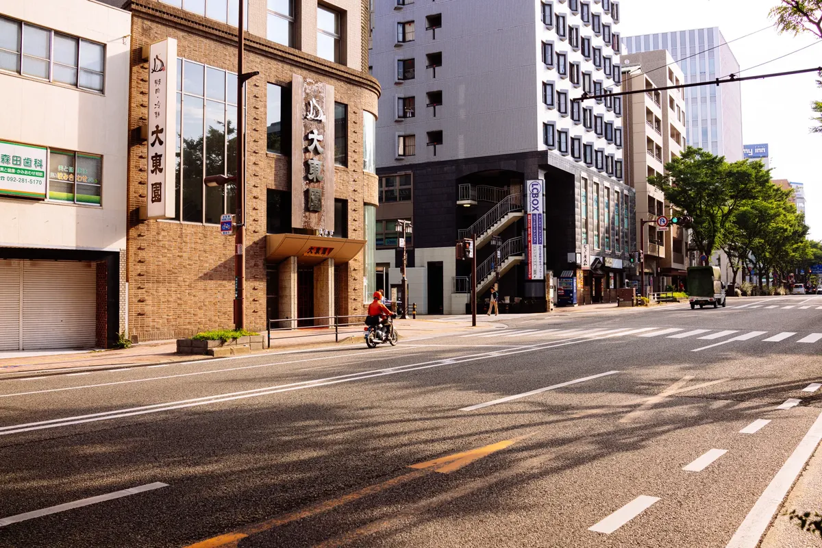 Sunny city street in Japan featuring modern architecture and a cyclist.