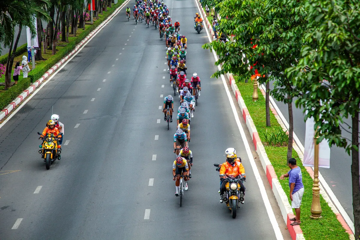 Aerial view of a cyclists' road race in a city during the day, showcasing teamwork and competition.